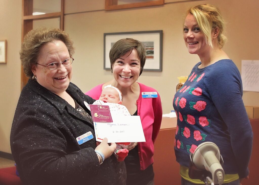 Two-week-old Elyana receives her first library card from friendly local librarians in Fergus Falls, MN.