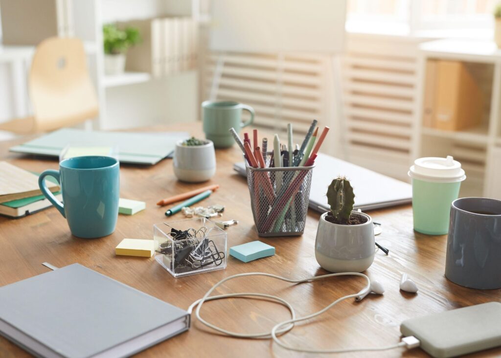 A cluttered homeschool desk covered in books, mugs, sticky notes, tangled cords, and scattered supplies, symbolizing the mental and physical chaos of burnout and overwork.