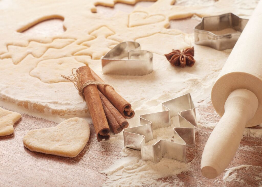 Rolled sugar cookie dough with flour, metal cookie cutters, cinnamon sticks, star anise, and a wooden rolling pin.