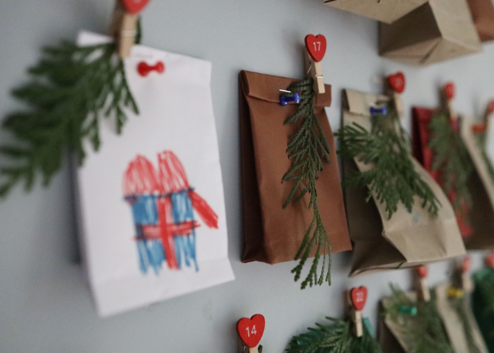 DIY Advent calendar with numbered clothespins, paper bags, evergreen sprigs, and a child’s hand-drawn gift.