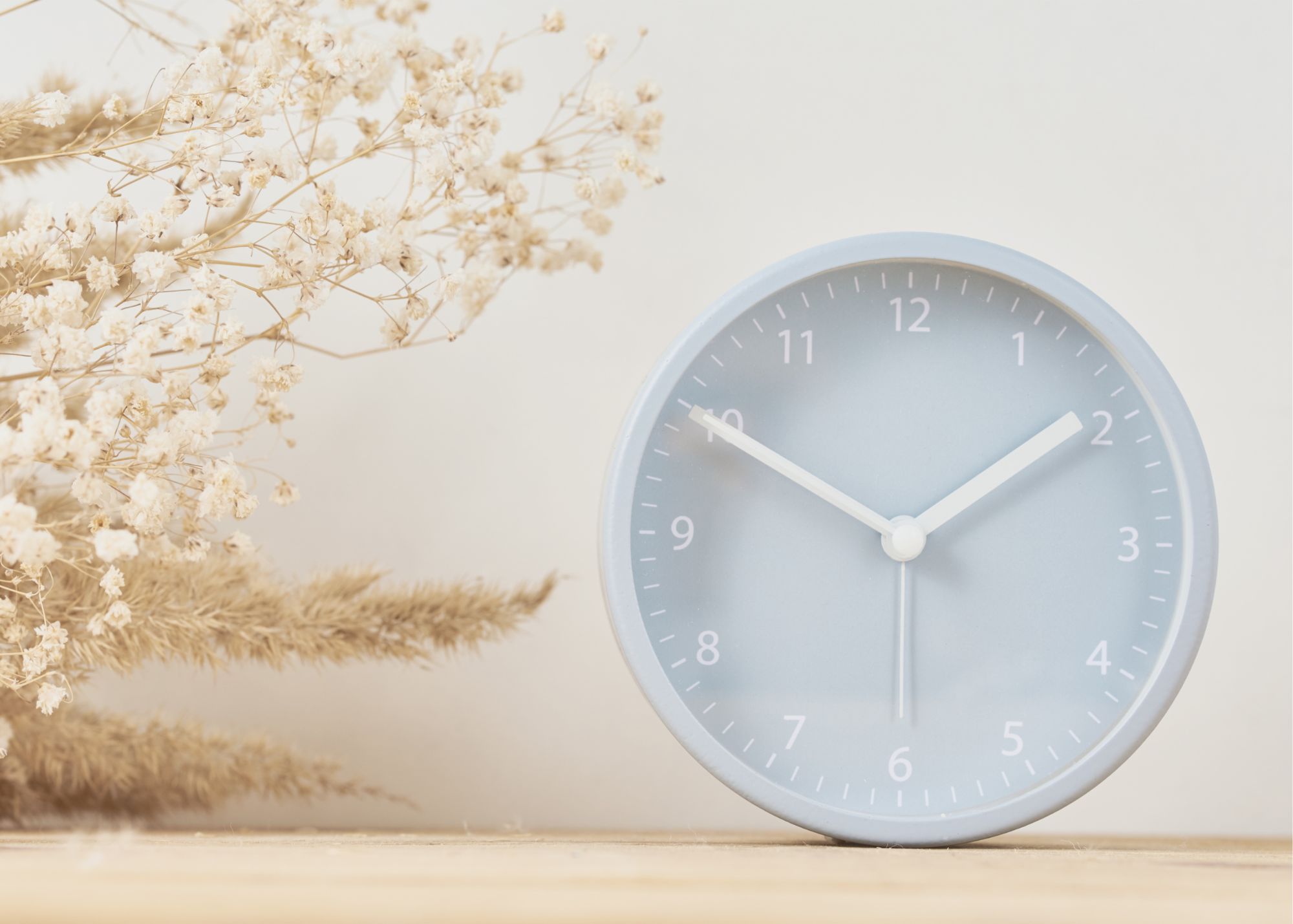 Minimal round desk clock on wood with dried flowers against a soft neutral background.