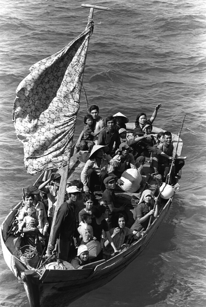 Black and white photograph of Vietnamese refugees crowded on a small wooden boat at sea, symbolizing the flight of the “boat people” during the late 1970s refugee crisis.