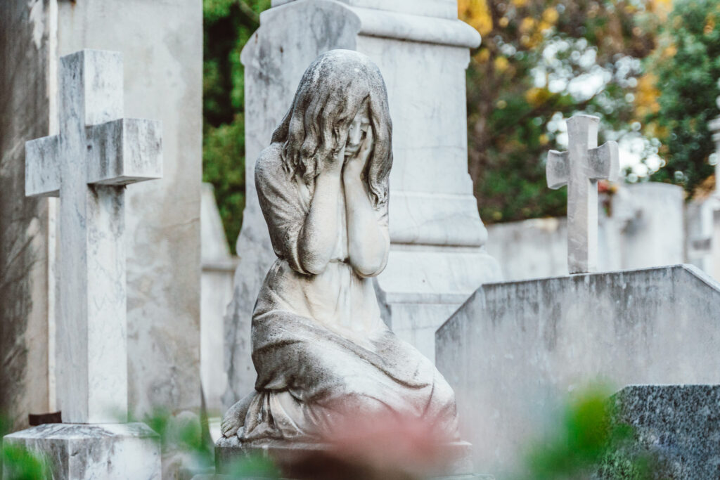 Marble statue of a woman weeping in a cemetery, flanked by stone crosses, evoking October grief and quiet lament.