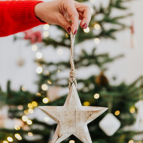 Hand holding a rustic star ornament near a Christmas tree, symbolizing Advent homeschool creativity.