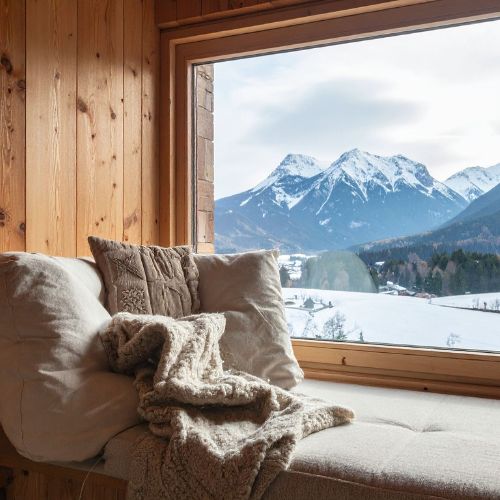 Cozy window seat with blankets and pillows overlooking snowy mountains, reflecting December creative homeschool ideas.