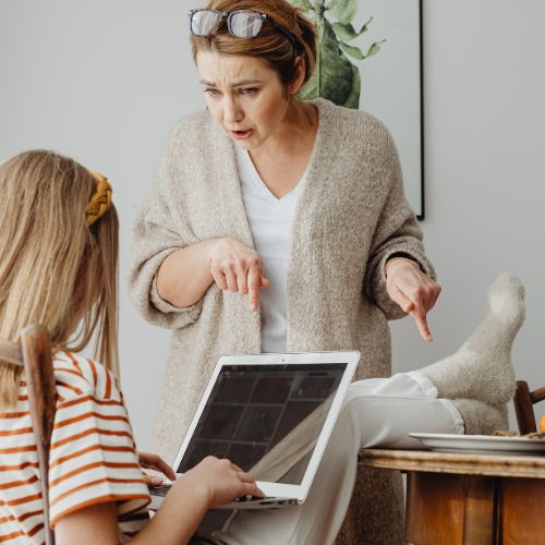 Mother guiding her frustrated teenage daughter during homeschool work on a laptop, representing logic stage homeschooling challenges.
